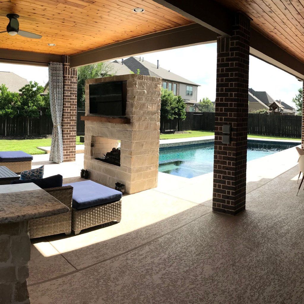 Covered patio with wicker seating, brick fireplace, and a backyard pool in bright sunlight