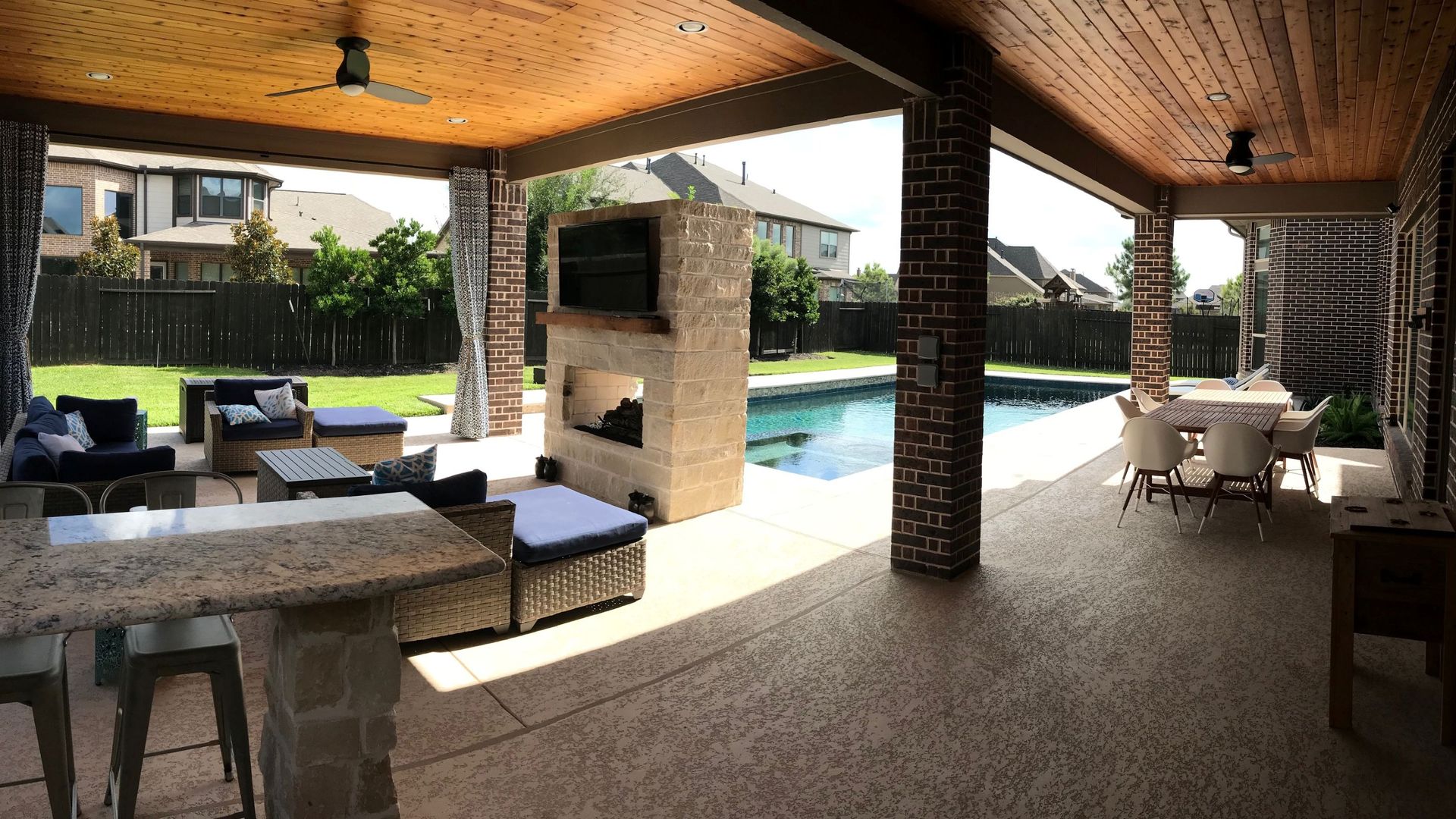 Covered patio with stone seating, bar, and a swimming pool in a backyard.