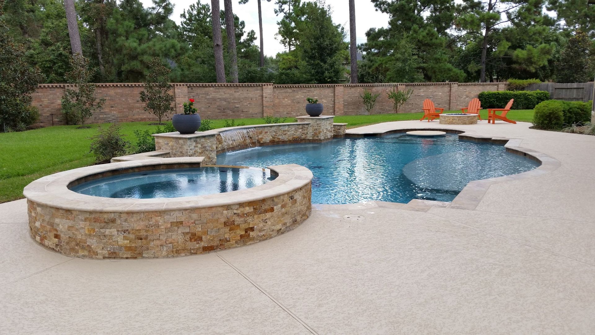 Backyard pool with attached hot tub, stone deck, and lounge chairs surrounded by greenery