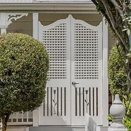 New Clients - Image: A white door with shutters on it is surrounded by trees and bushes .