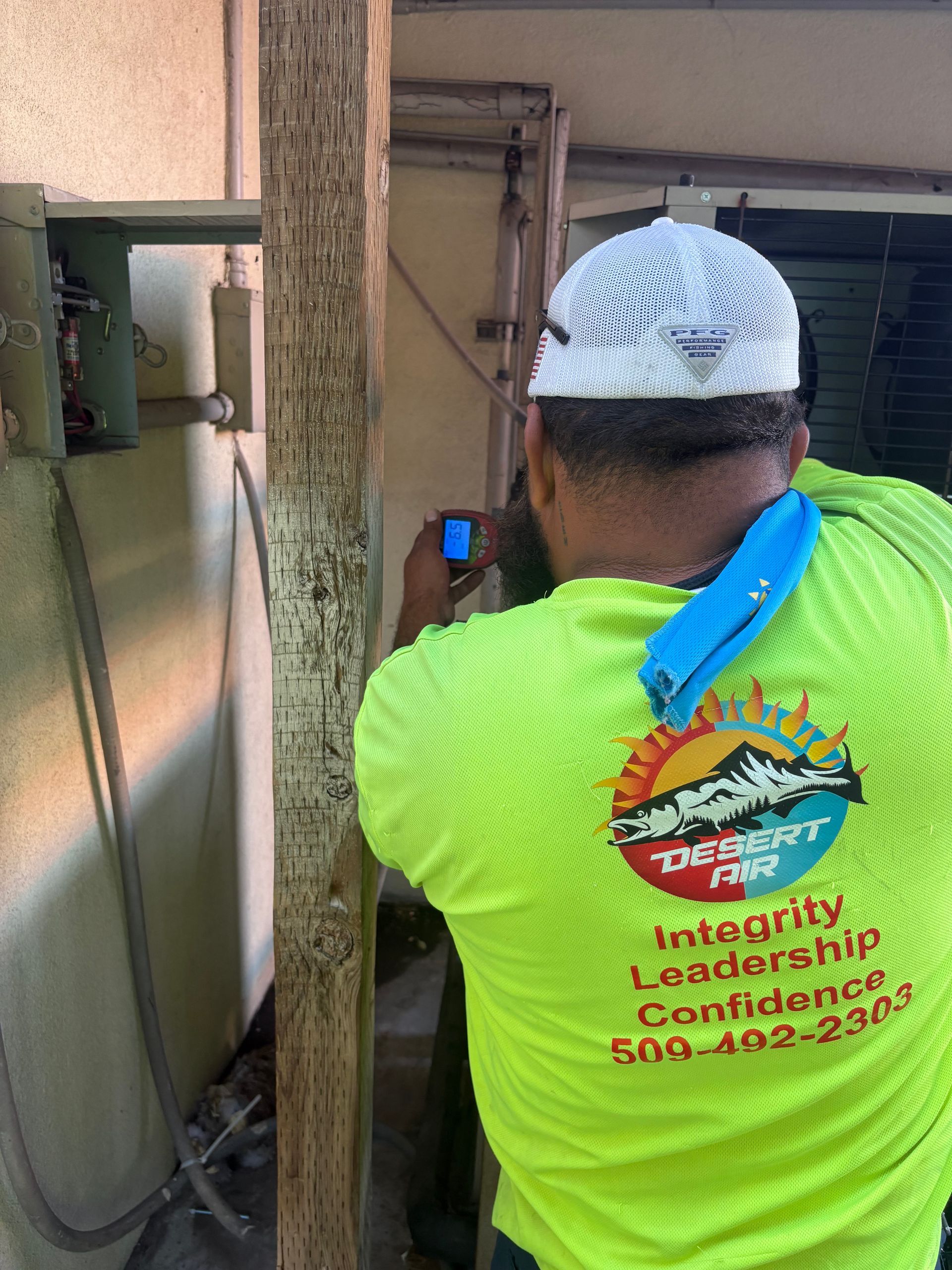 Worker in neon green shirt using a tool near outdoor equipment by a wall