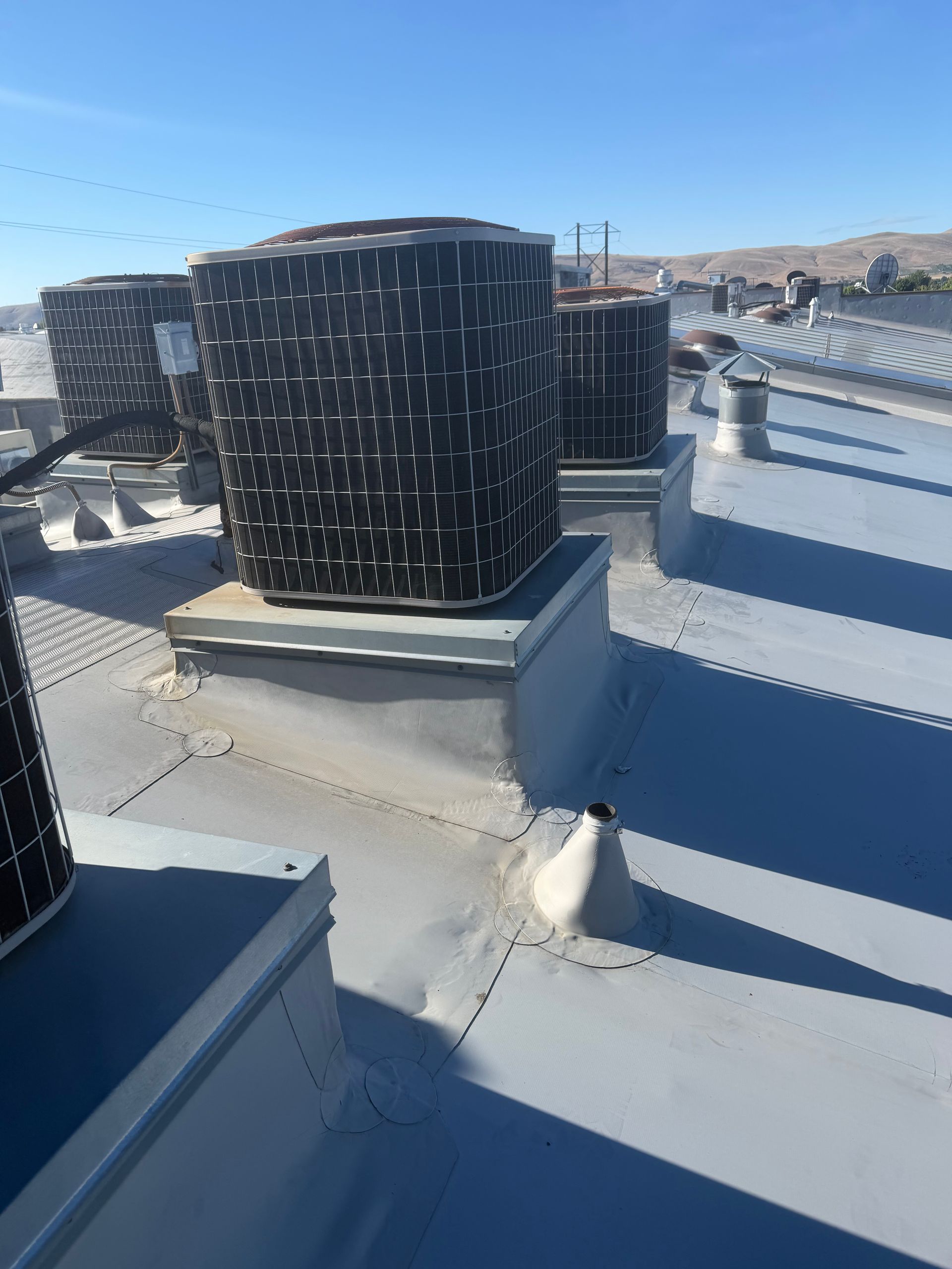 Rooftop HVAC units on a white commercial roof under a clear blue sky