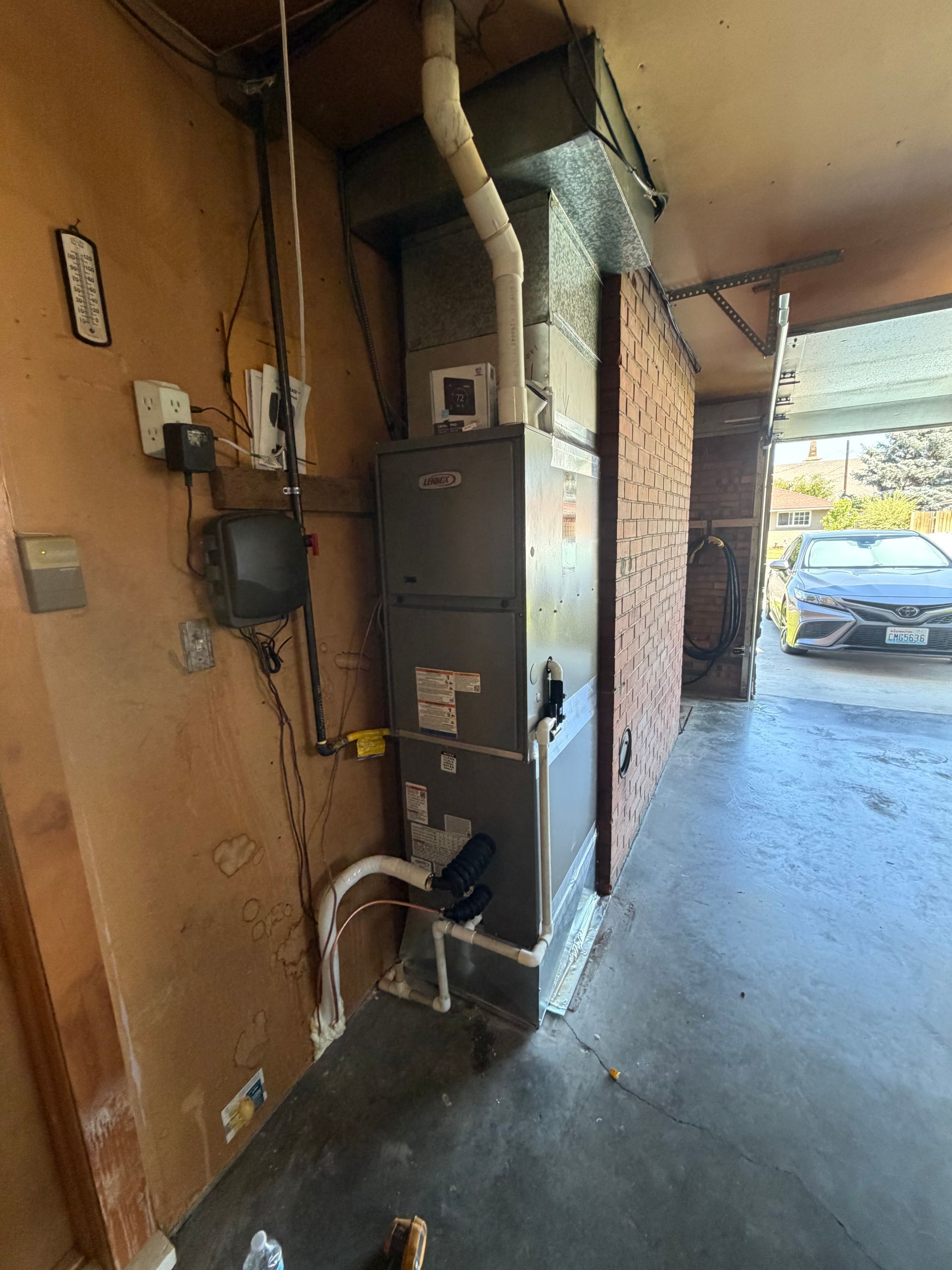 Utility meters and electrical boxes mounted on a wall in a covered outdoor walkway, with a car in the background.