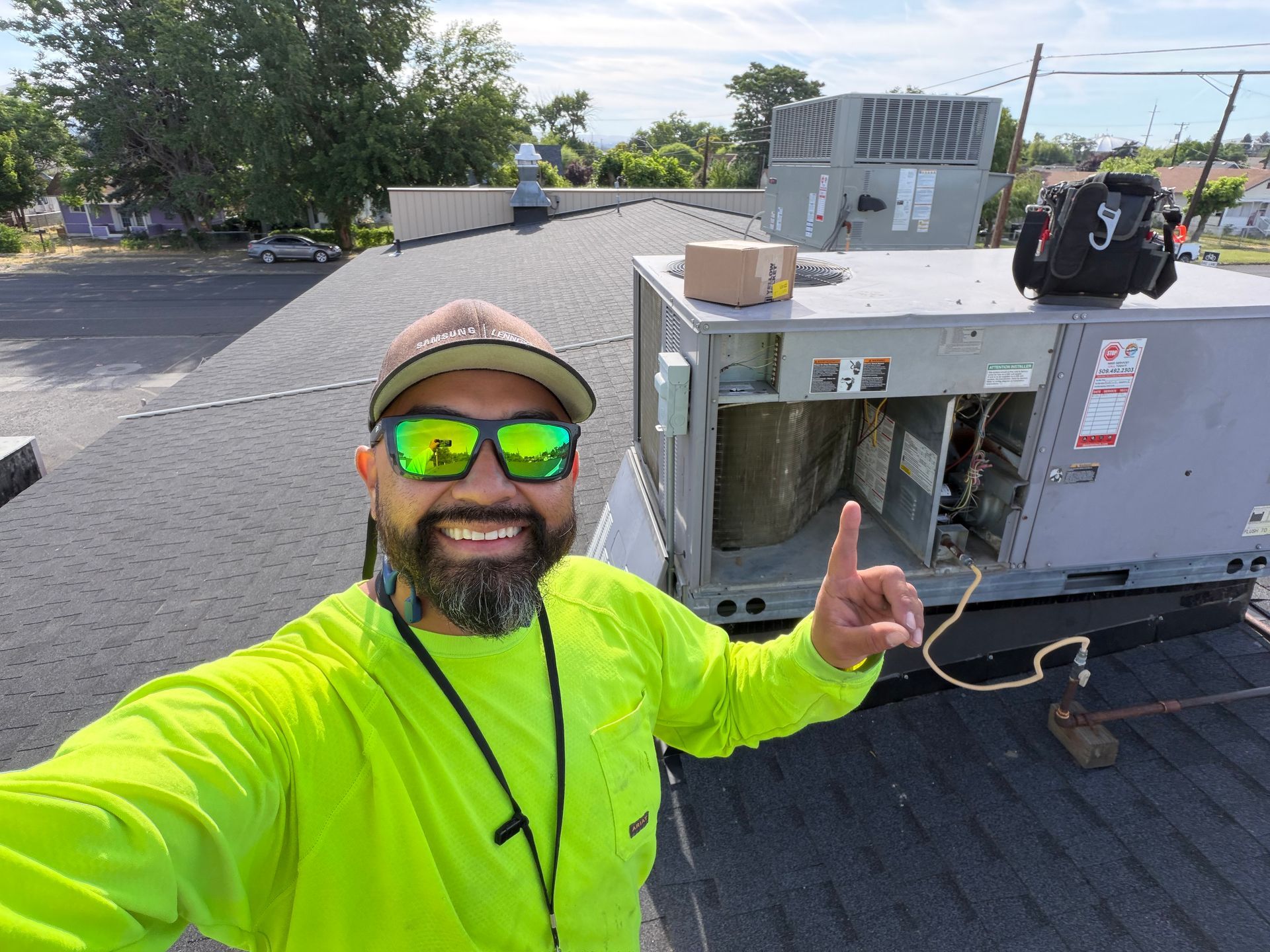 Person in neon yellow shirt and cap smiling on a rooftop beside HVAC equipment, giving a thumbs-up.