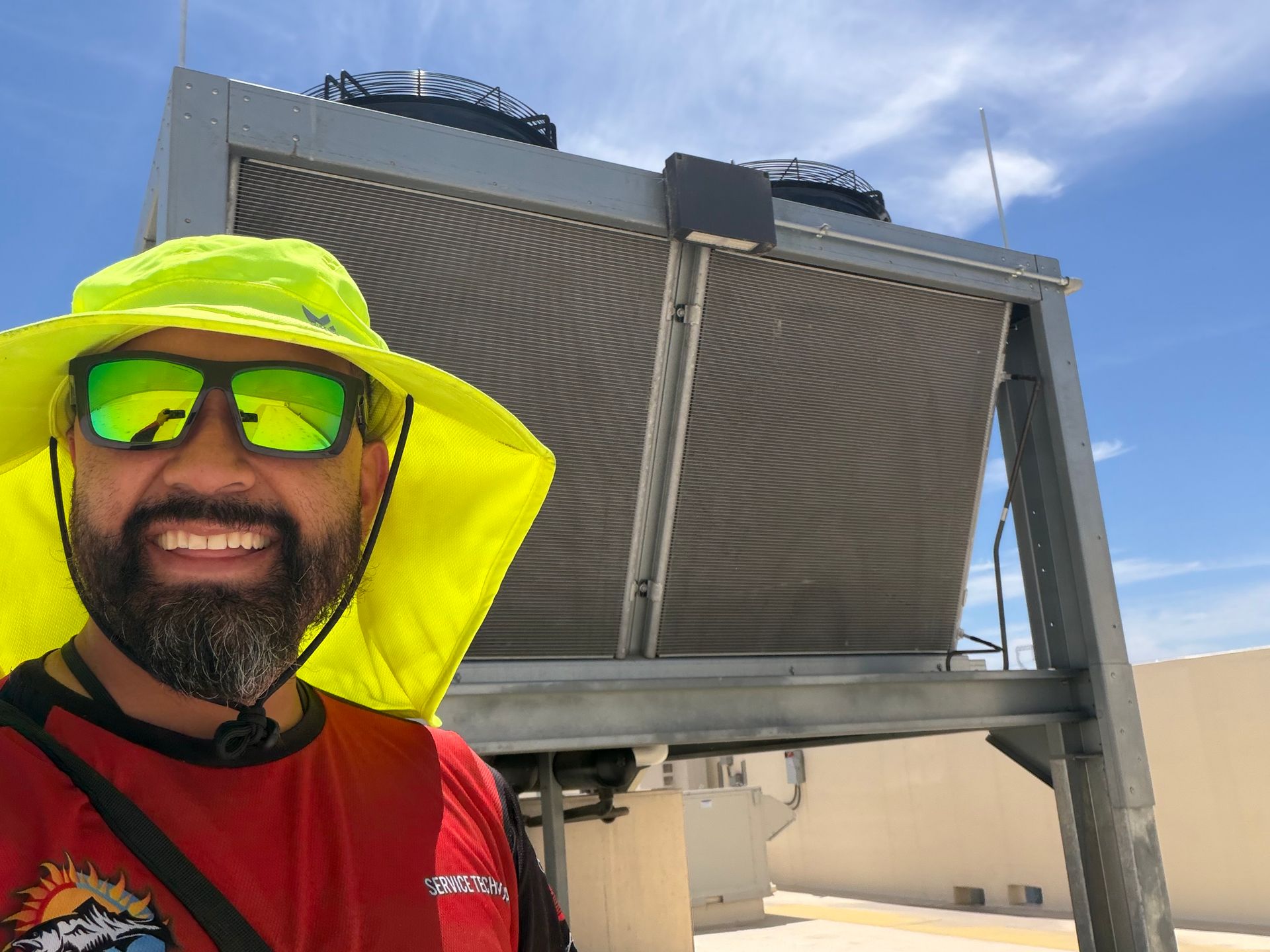 Man in neon yellow hat and sunglasses posing before large rooftop solar panels under a blue sky