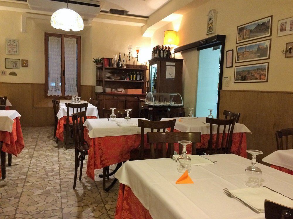 Accogliente sala da pranzo di un ristorante con tovaglie bianche, dettagli rossi e quadri incorniciati alle pareti.
