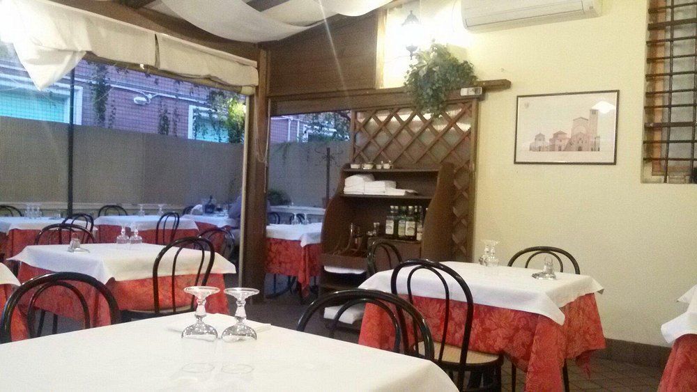 Sala da pranzo vuota di un ristorante, con tovaglie a quadri bianchi e rossi e sedie nere sotto un baldacchino.