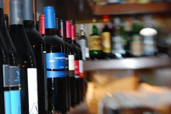 Bottiglie di vino allineate su uno scaffale da bar, con una bottiglia dall'etichetta blu in primo piano.