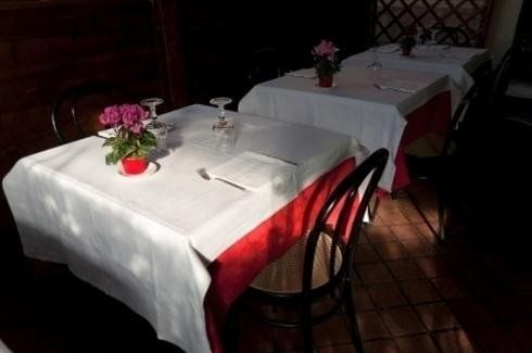 Tavoli di ristorante scarsamente illuminati con tovaglie bianche, tovaglioli rossi e piccoli vasi di fiori disposti in fila