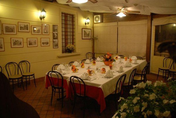 Sala da banchetto scarsamente illuminata con un lungo tavolo da pranzo, sedie, quadri alle pareti e fiori.