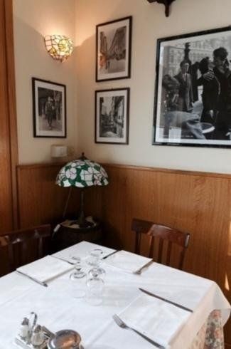 Accogliente angolo ristorante con un tavolo apparecchiato con una tovaglia bianca, sedie in legno, opere d'arte alle pareti e una lampada in vetro colorato.