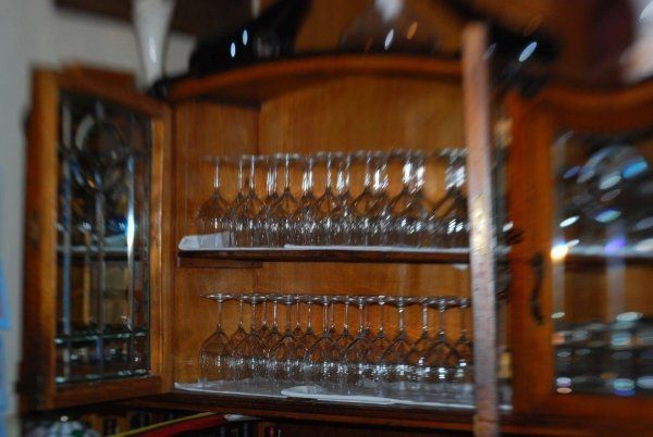 Bicchieri e oggetti in vetro esposti su scaffali di legno all'interno di una vetrina, con file di bicchieri con stelo e caraffe.