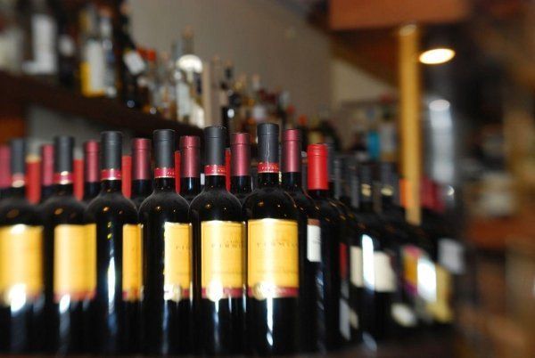 File di bottiglie di vino con tappi rossi su uno scaffale da bar, leggermente sfocate sullo sfondo.