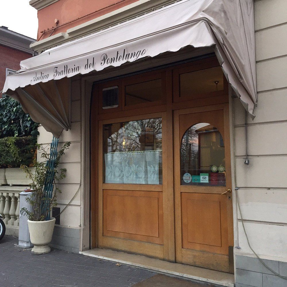 Esterno di una piccola panetteria con tenda da sole beige e doppie porte in legno, situata in una strada tranquilla.