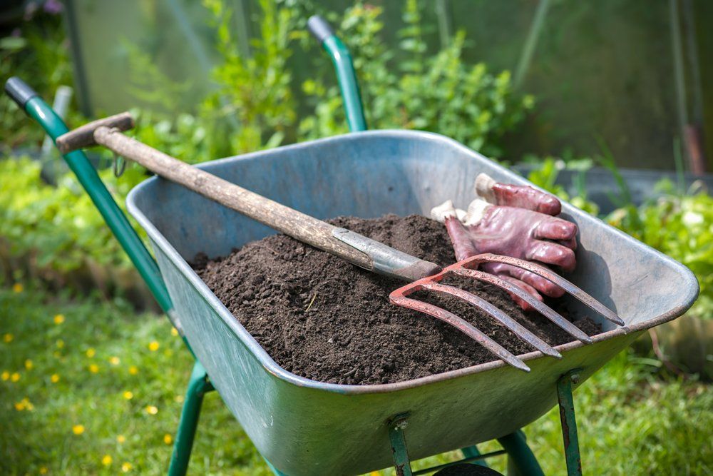 A Wheelbarrow Filled with Dirt and A Shovel and Rake — All Round Ground Maintenance in Bellingen, NSW