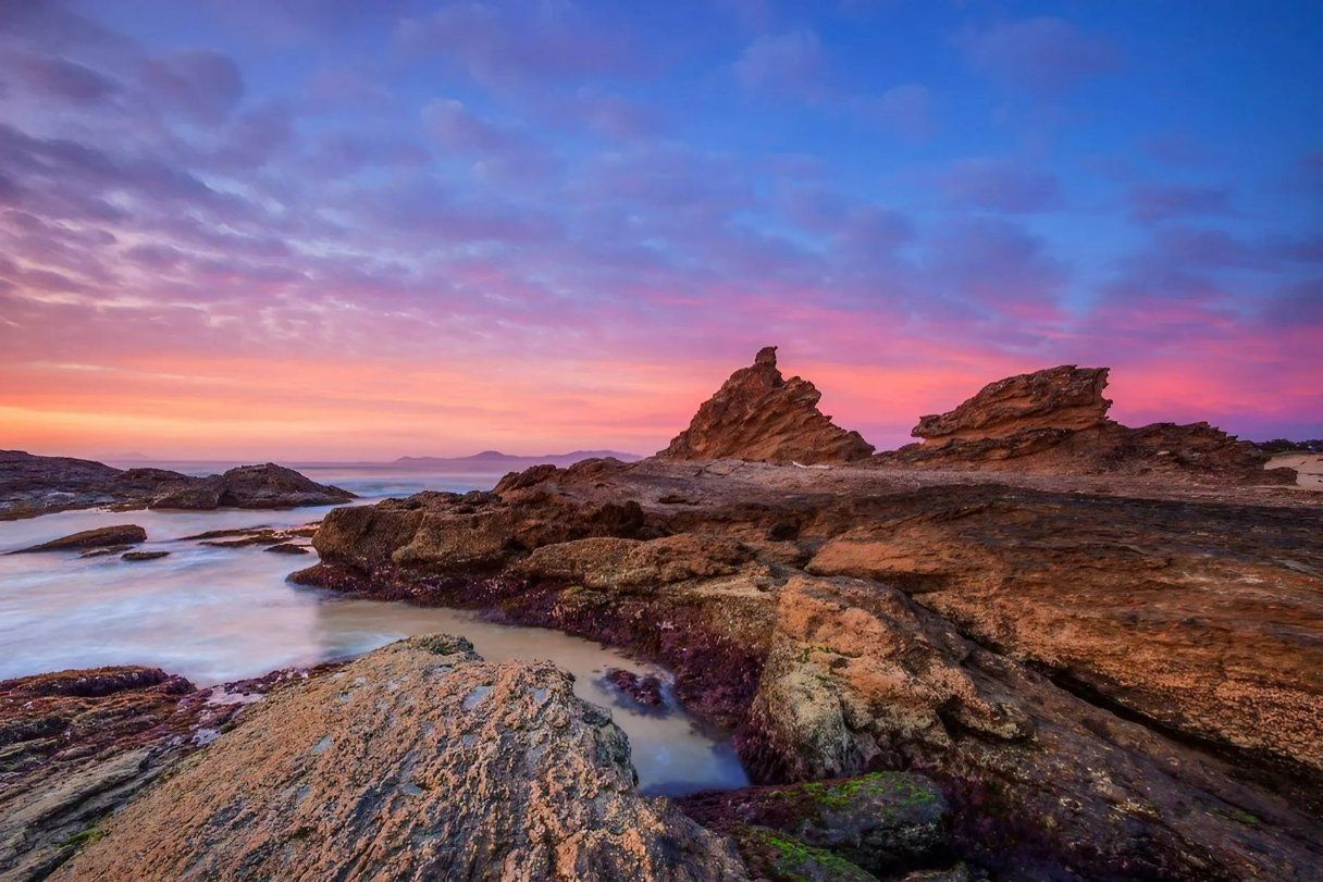A Sunset Over a Rocky Beach with A Large Rock in The Foreground — All Round Ground Maintenance in Mid North Coast, NSW