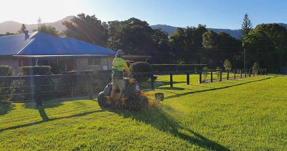 A Man Is Riding a Lawn Mower on A Lush Green Field — All Round Ground Maintenance in Mid North Coast, NSW