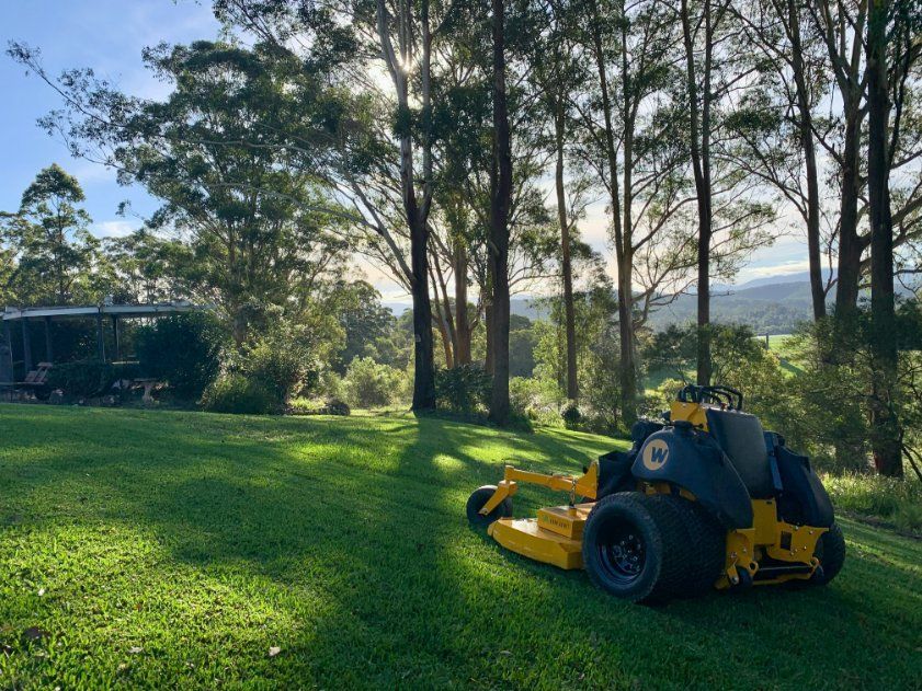 A Yellow Lawn Mower Is Parked in The Middle of A Lush Green Field — All Round Ground Maintenance in Urunga, NSW