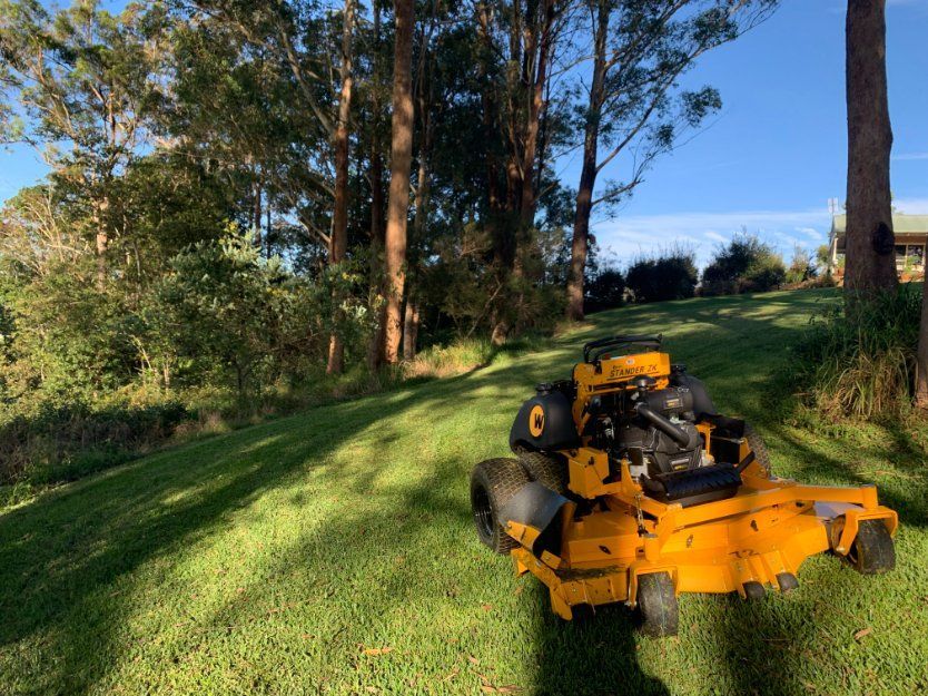 A Yellow Lawn Mower Is Sitting on Top of A Lush Green Lawn — All Round Ground Maintenance in Bellingen, NSW