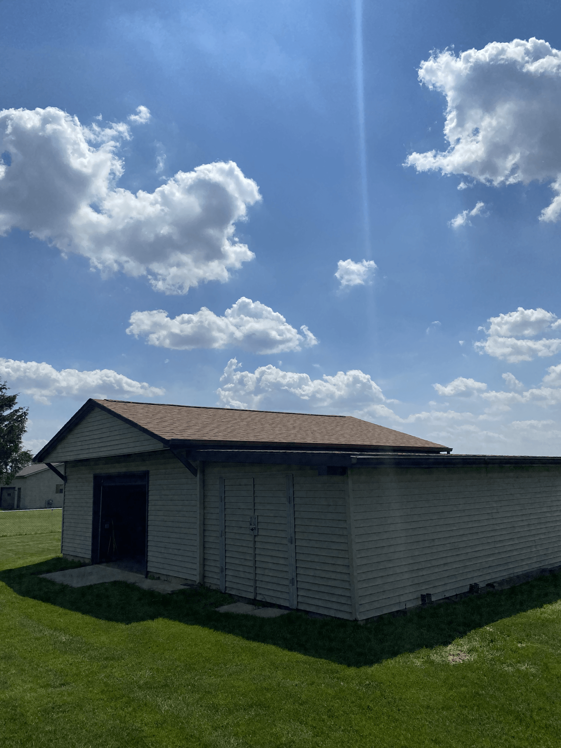 A white garage with a brown roof is sitting in the middle of a grassy field.