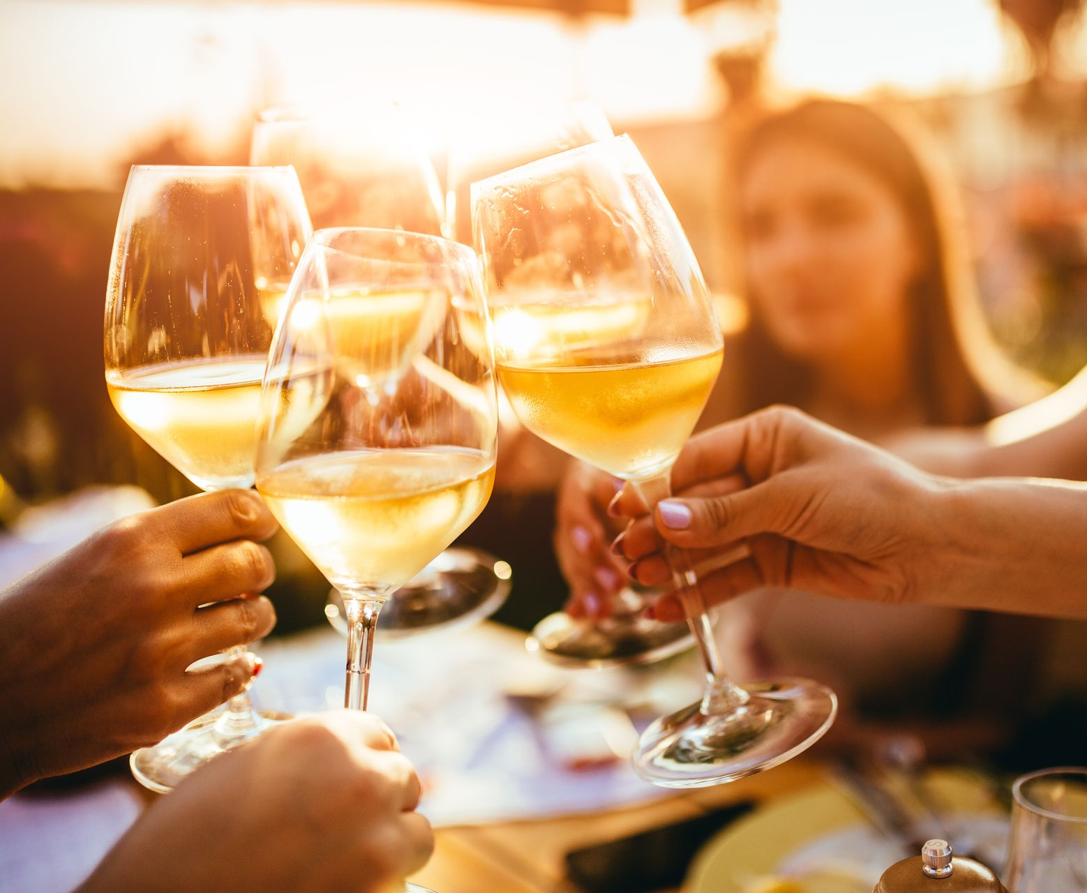 Hands raising glasses of white wine in a warm, sunlit outdoor toast