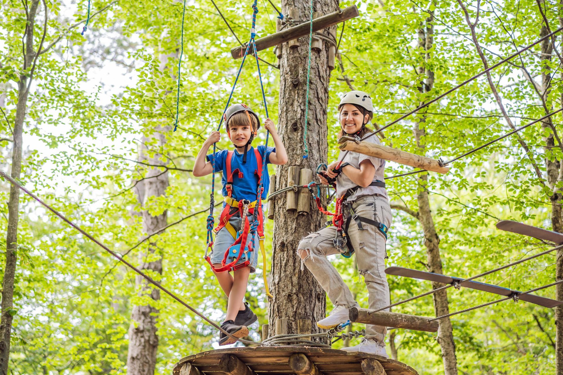 Two climbers in helmets and harnesses on a ropes course in a green forest