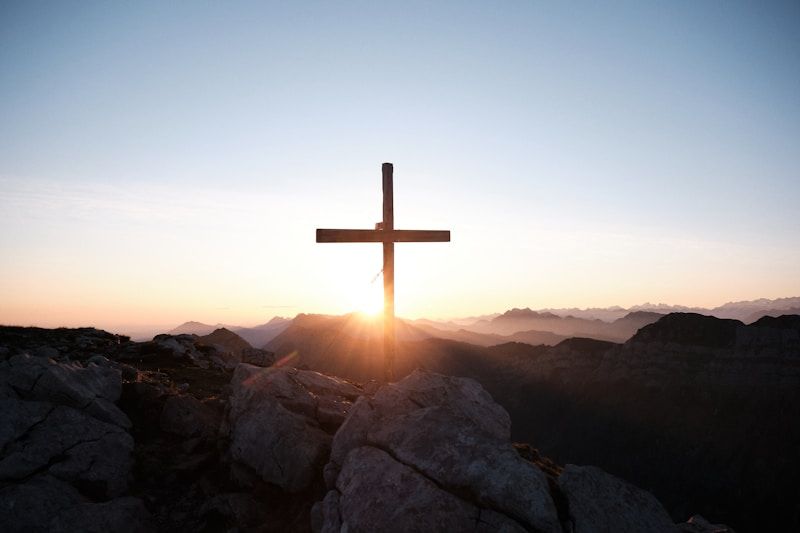 Cross silhouetted at sunrise over rocky hills and misty mountains