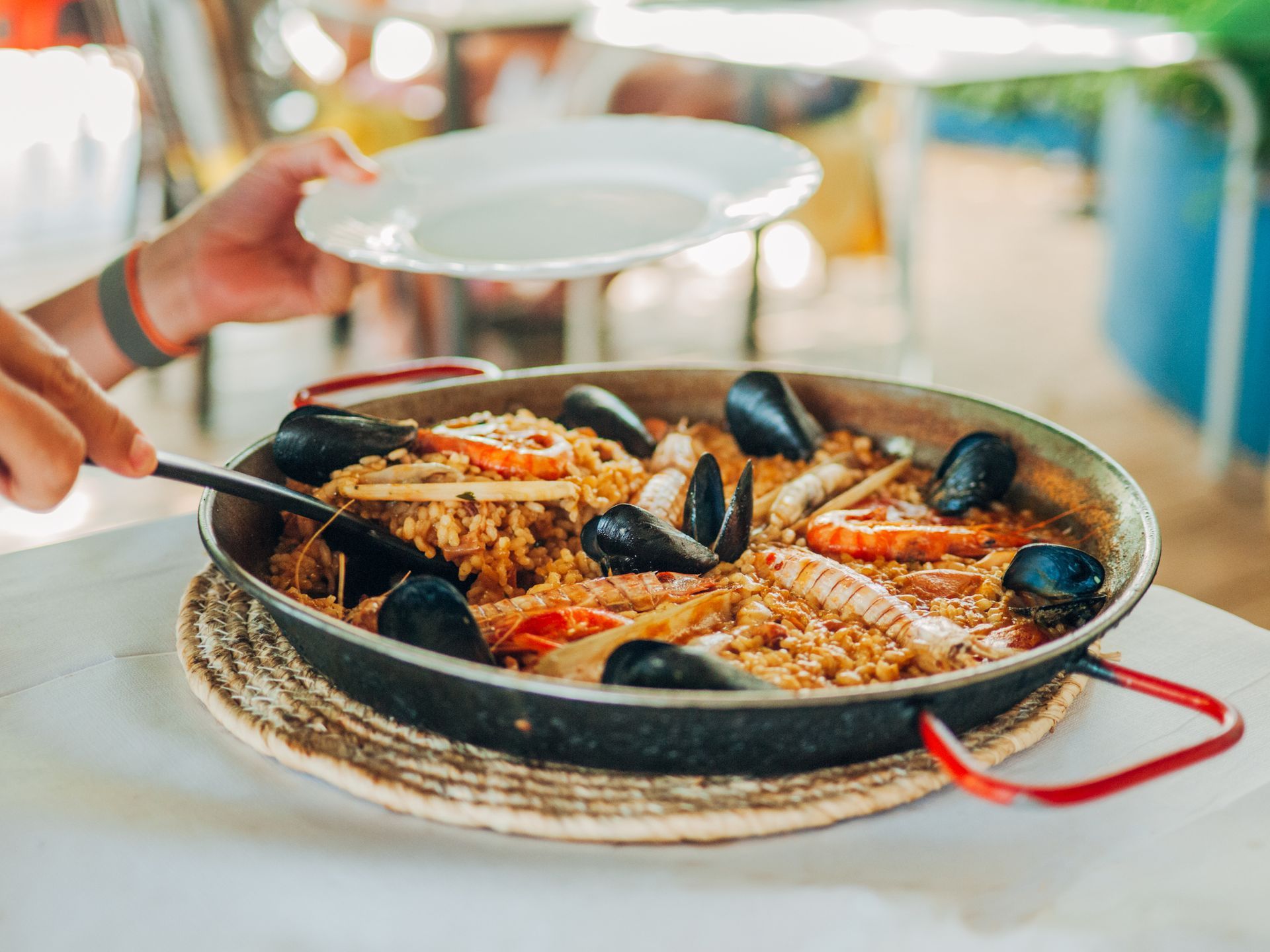 Una persona prende un cucchiaio di paella da una padella.