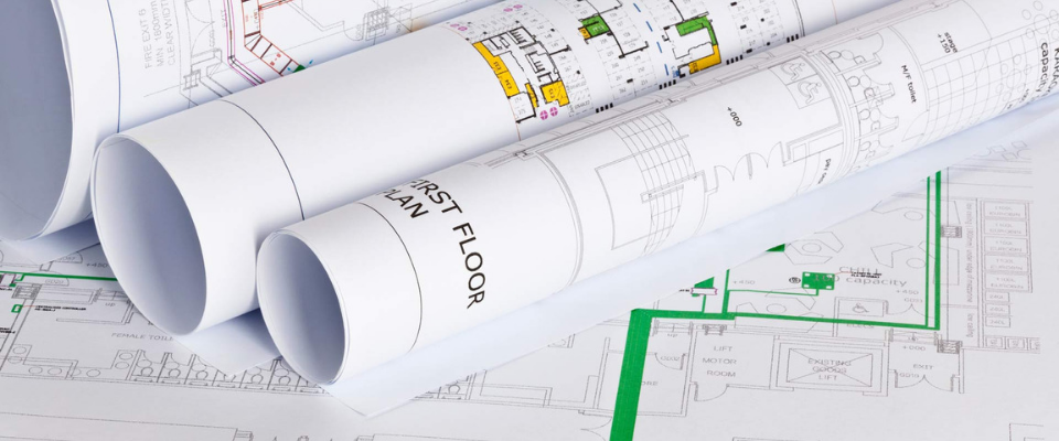 Rolled architectural blueprints with technical floor plans and green utility markings resting on a flat drawing.