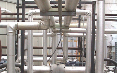 An industrial setting with numerous insulated silver metal pipes arranged in a complex grid.