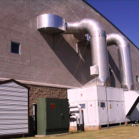 Large HVAC industrial units outside a block building with two prominent metal ventilation ducts attached to the wall.