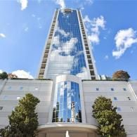 A modern, tall glass skyscraper against a bright blue sky with wispy white clouds, featuring a stone entrance below.