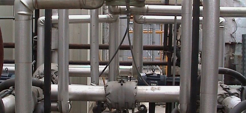 A close-up of a complex network of industrial metal pipes and insulation in a mechanical or utility setting.