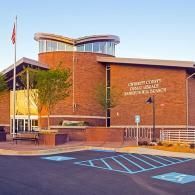 A red brick Gwinnett County public library branch with a curved glass clerestory and a blue-striped accessible parking spot.