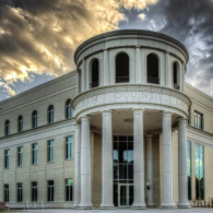 A Neoclassical building with a grand, pillared stone rotunda entrance against a dramatic, cloudy sunset sky.