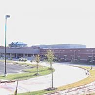 A wide-angle exterior view of a low-rise brick school building featuring a curved driveway and parking lot.