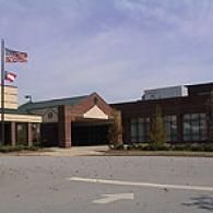 A brick building entrance with a flagpole displaying the American and Georgia flags under a blue sky.