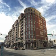 A curved, multi-story brick building on a city street corner with arched ground-level storefronts under a cloudy sky.