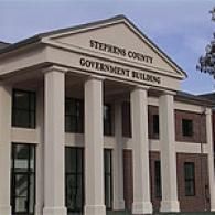 The Stephens County Government Building featuring a portico with white columns and a red brick exterior under a blue sky.