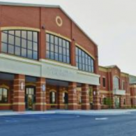 A modern brick commercial building with large windows, an overhang entrance, and a paved parking lot.