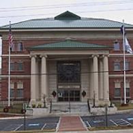 A three-story brick government building with a green roof, fronted by a large stone portico with four prominent columns.