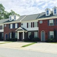 A multistory red brick and white-sided apartment building with dark roofs, dormer windows, and covered entrances.