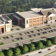 An aerial view of a multi-story brick school building with a large parking lot and surrounding greenery.