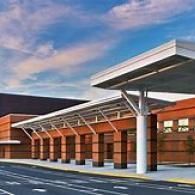 A modern brick building exterior featuring a long, covered walkway with a large, white support pillar under a blue sky.