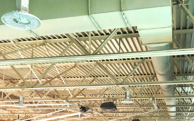 Industrial ceiling featuring metal roof trusses, exposed ventilation ductwork, and hanging light fixtures.