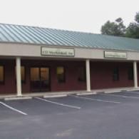A one-story brick commercial building with a green metal roof and a parking lot in front.