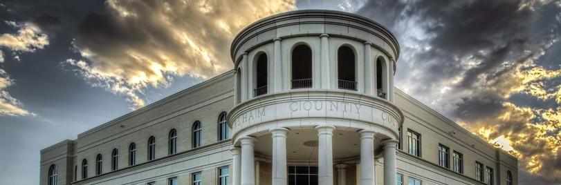 The light-colored, classical-style building features a prominent rounded portico with columns under a dramatic, cloudy sky.
