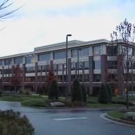 A multistory, red-brick office building with a modern facade and reflective glass windows, surrounded by trees and a road.