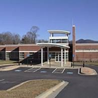 A modern, brick building with a white curved canopy entrance, a prominent central tower, and an empty parking lot.