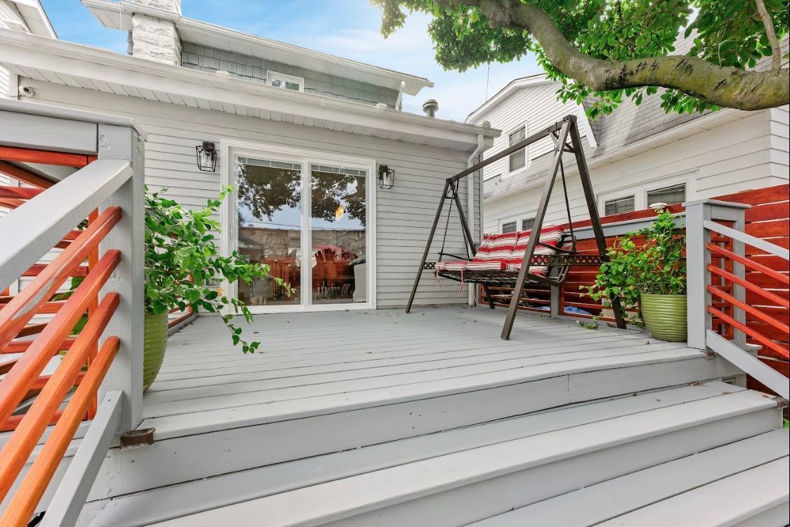 There is a swing on the deck of a house.